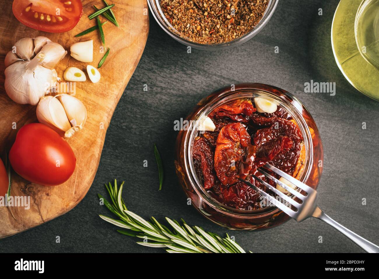 Cuisine des tomates séchées dans un pot en verre avec huile d'olive, ail et romarin, vue sur le dessus, plat. Banque D'Images