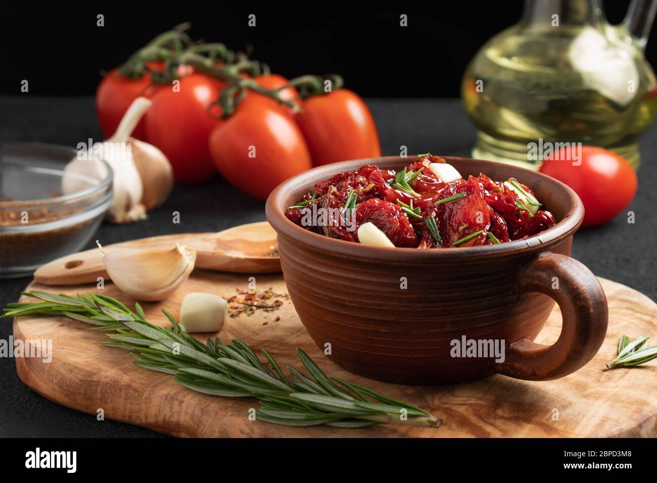 Tomates séchées au soleil avec ail, romarin et épices dans un bol en argile sur un tableau de découpe en bois d'olive. Banque D'Images