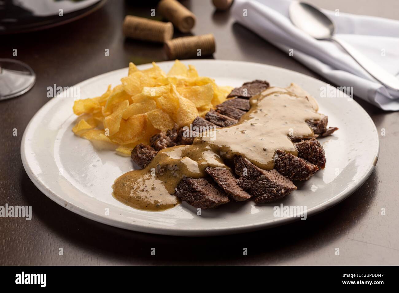 Steak avec sauce avec chips de pomme de terre sur une assiette blanche et verre à vin, liège, couverts et serviette Banque D'Images