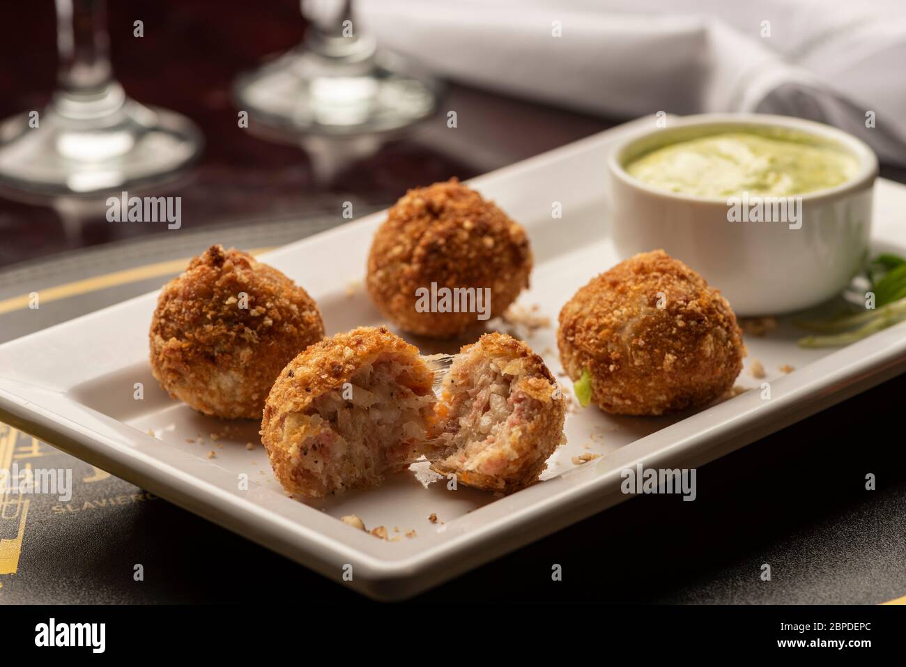 billes d'arancini farcies de fromage sur une assiette blanche, verres à vin et serviette Banque D'Images