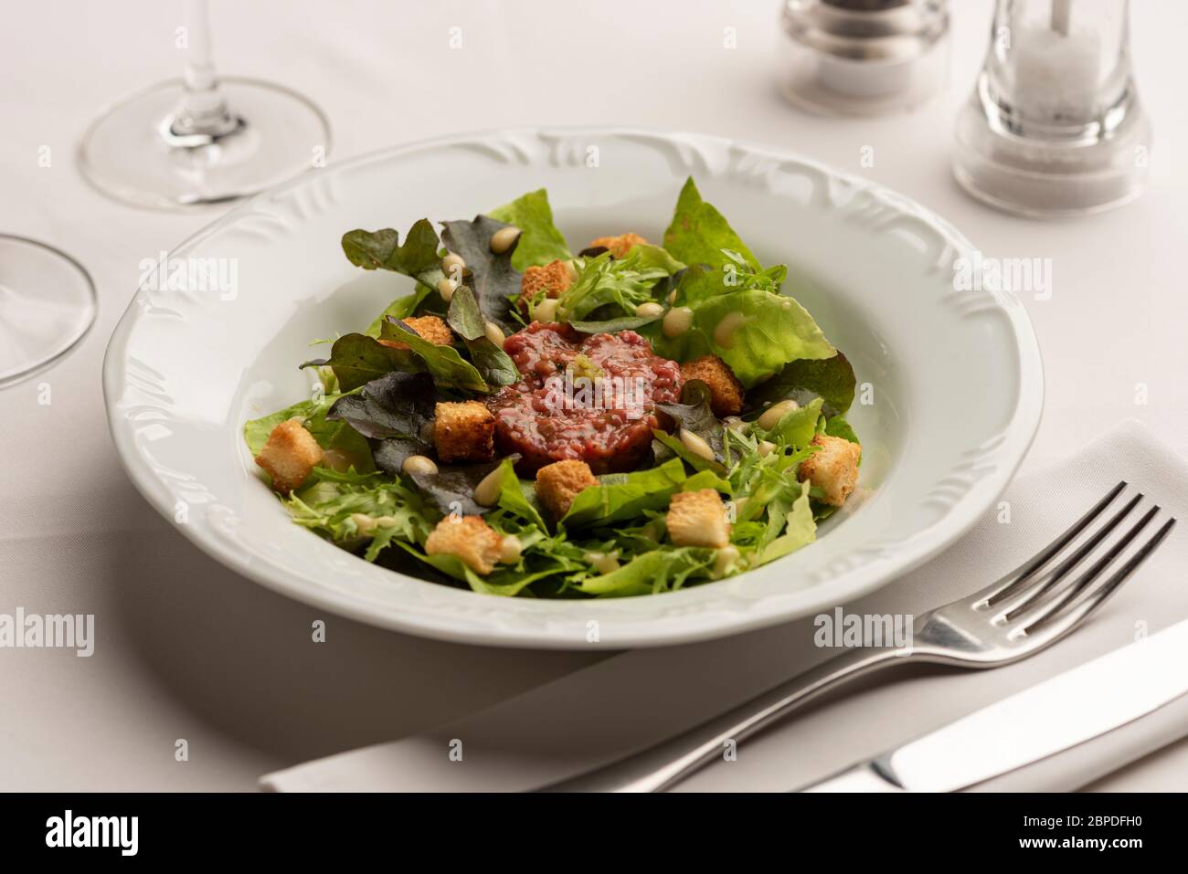 Salade verte avec tomates laitue sur fond blanc flou avec verres à vin, vinaigre et huile d'olive. Banque D'Images