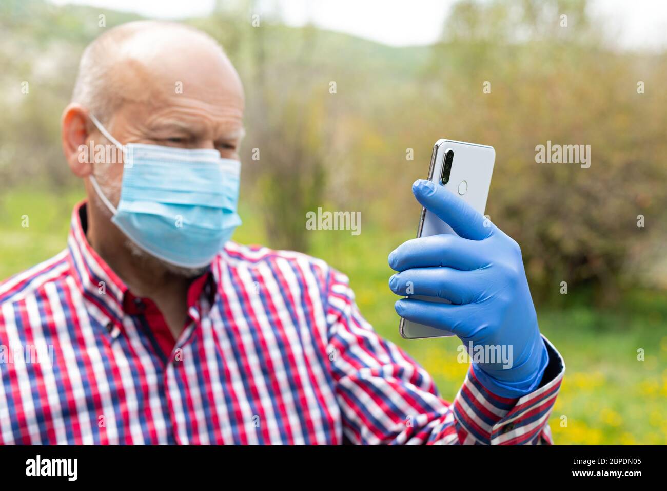 Portrait d'un homme âgé portant un masque chirurgical et des gants parlant au téléphone à l'extérieur Banque D'Images