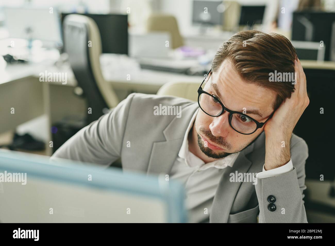 Un jeune homme d'affaires stressé travaillant seul au bureau et regardant les statistiques de ventes négatives sur le moniteur informatique pendant la pandémie du coronavirus Banque D'Images