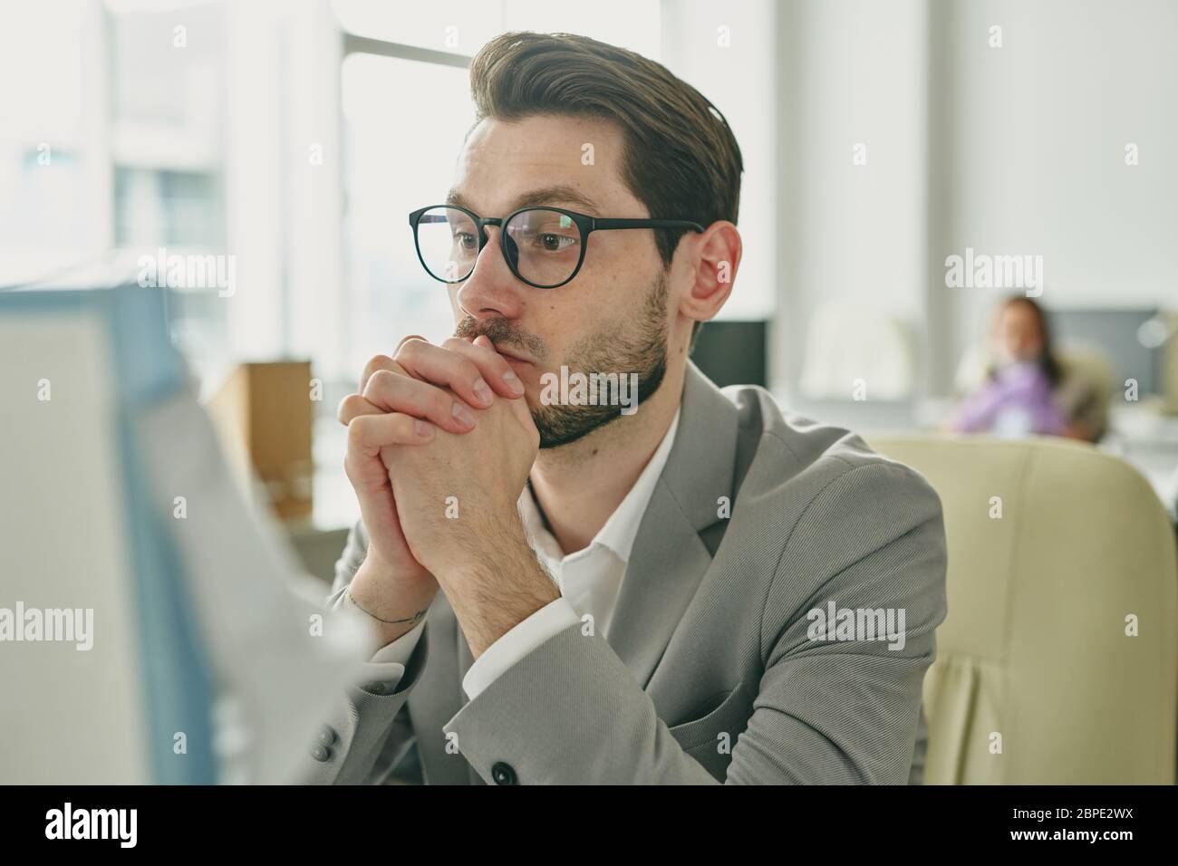 Un jeune homme d'affaires barbu concentré se penchait sur les mains et regardait un écran d'ordinateur tout en priant pour conclure un accord pendant le coronavirus Banque D'Images