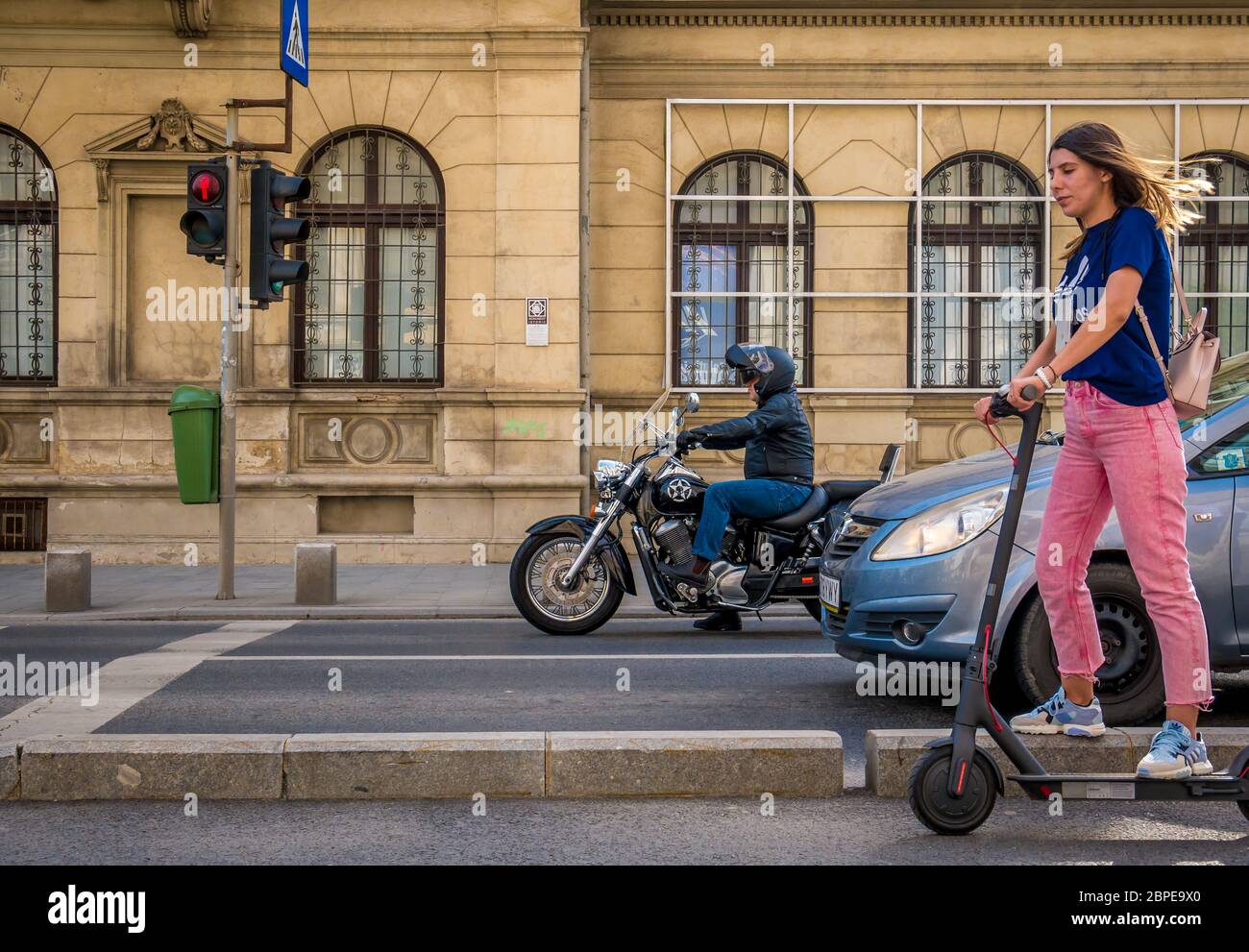 Bucarest/Roumanie - 05.16.2020: Un cycliste sur une moto et une fille trigant un scooter électrique au feu de circulation. . Les gens qui apprécient une belle journée dans le ce Banque D'Images