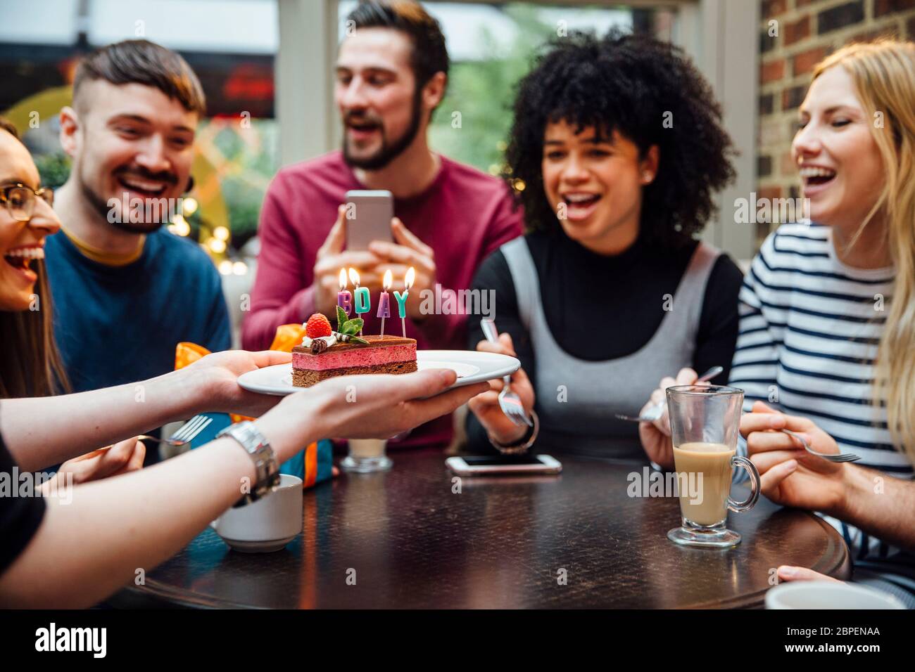 Groupe d'amis sont dans un bar célèbre de la femme sur les anniversaires des enfants. Quelqu'un qui fait un dessert avec des bougies qui sort "BDAY" en lui. Banque D'Images