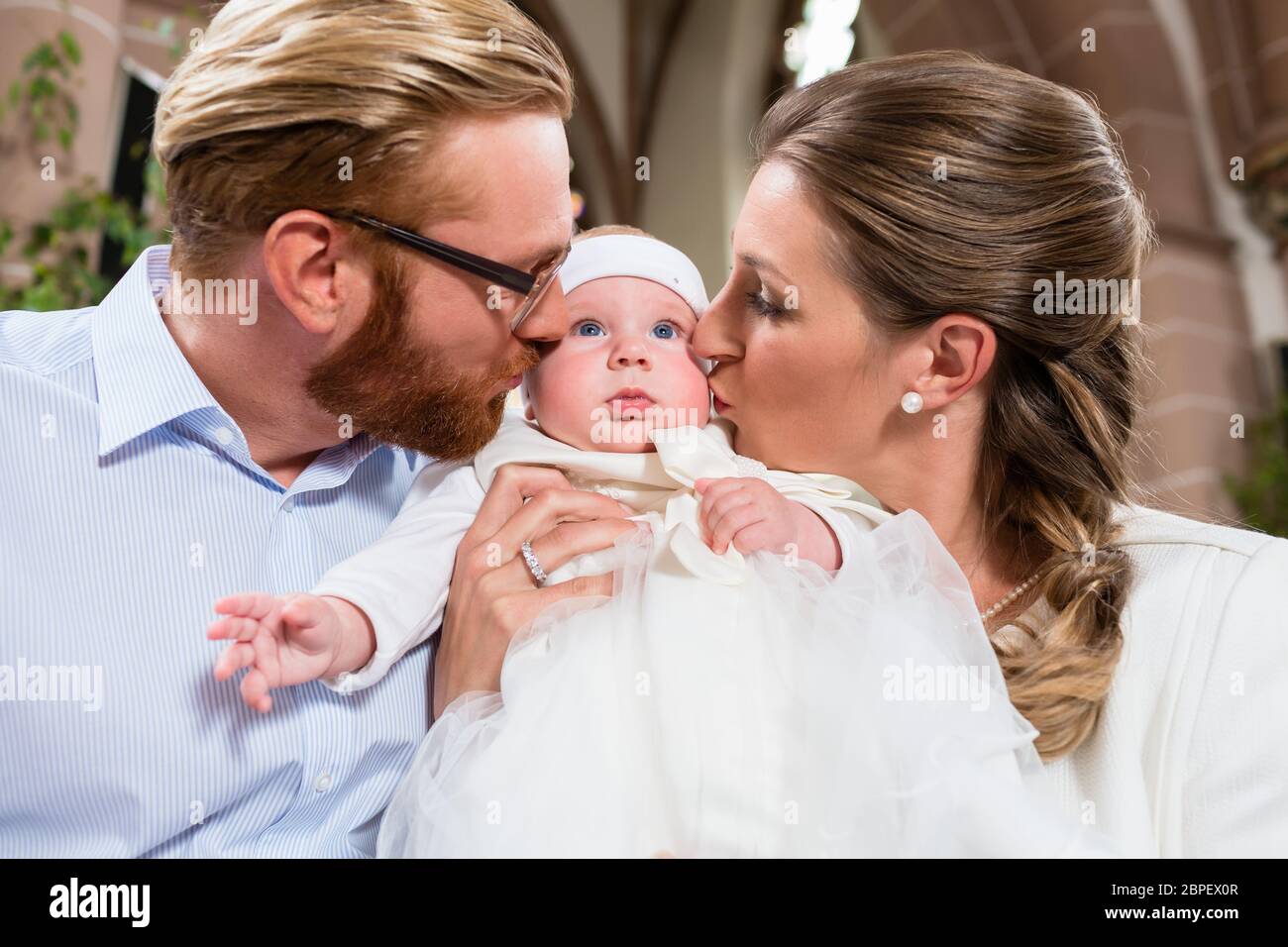 Les jeunes parents baiser leur bébé en même temps après la cérémonie du baptême Banque D'Images