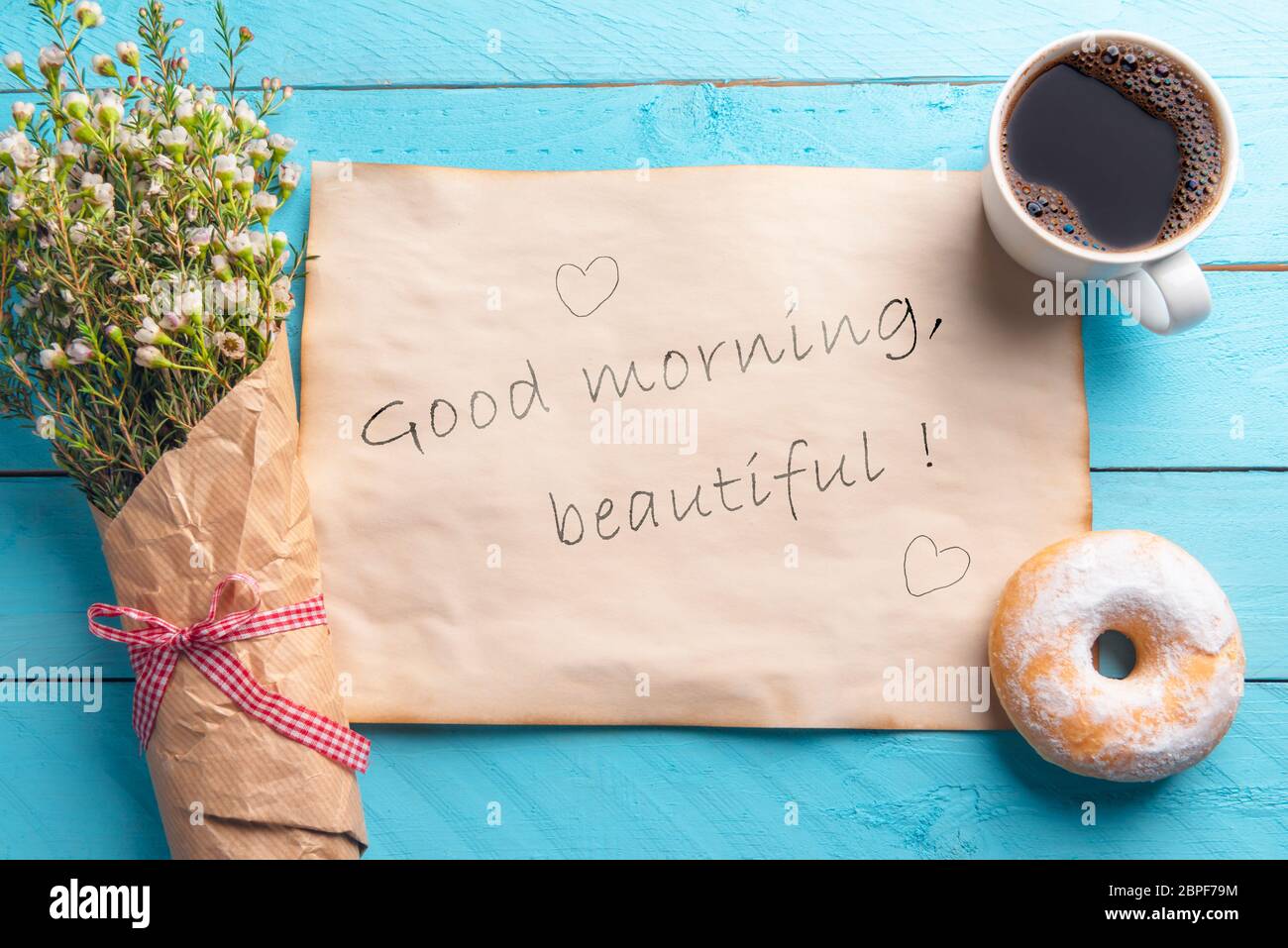 Vintage papier avec le bon matin beau message et le cœur, un bouquet de fleurs de printemps, un café chaud, et donut, sur un fond bleu en bois. Banque D'Images