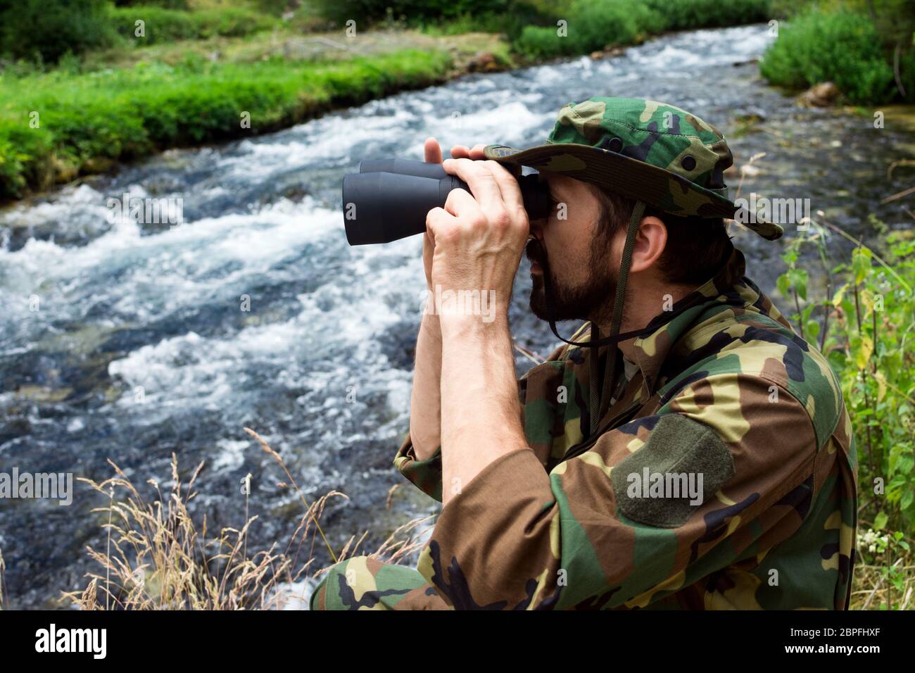 Le naturaliste en uniforme militaire avec des jumelles est en mission  d'observation des oiseaux dans la nature au bord de la rivière Photo Stock  - Alamy