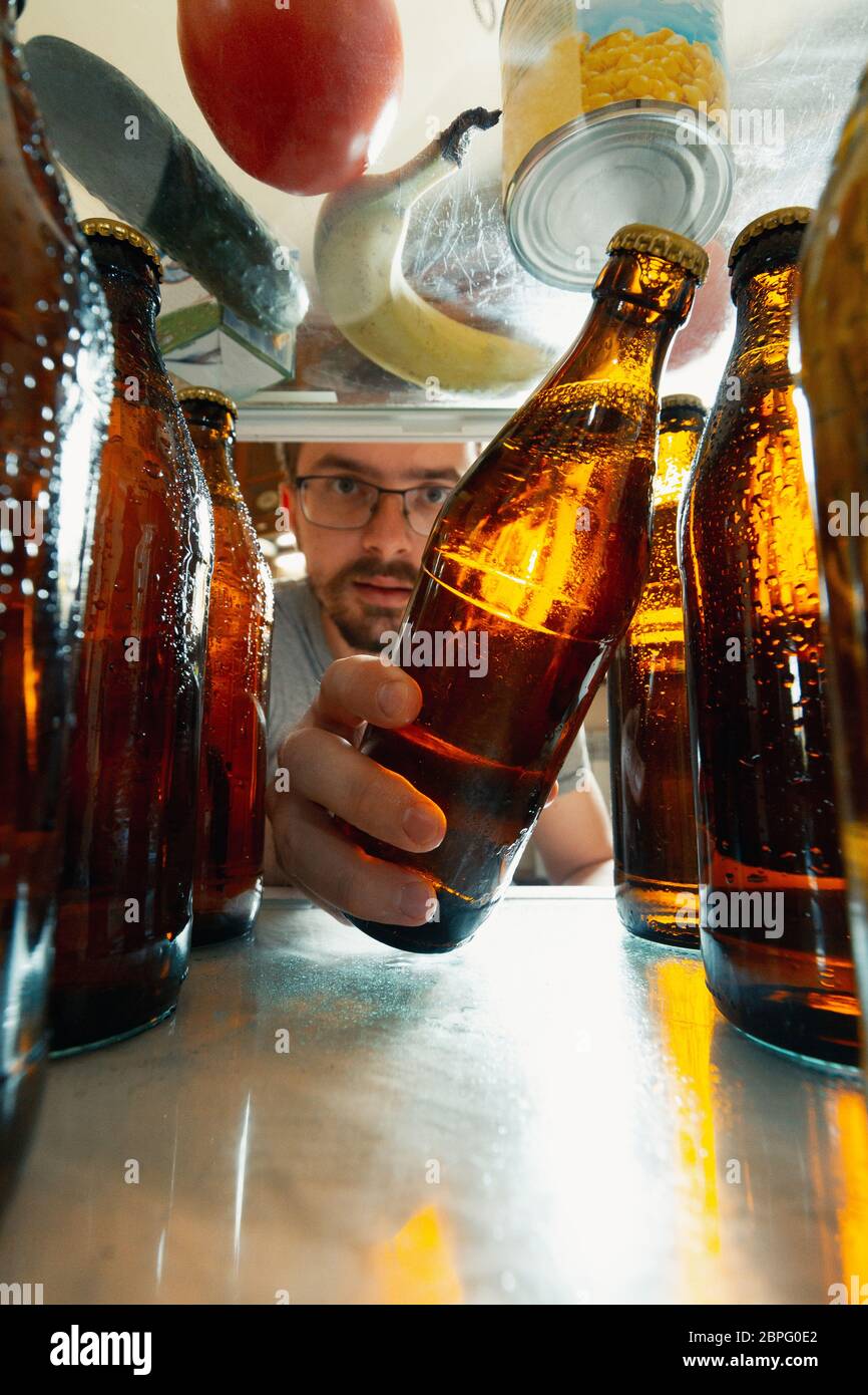 Homme caucasien prend la bière fraîche rafraîchissante hors du  réfrigérateur, vue intérieure du réfrigérateur de tenir la bouteille à la  main. Alcohole, vie domestique, divertissement, concept de boisson.  Bouteilles de bière ou