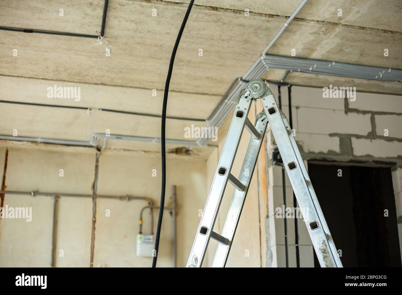 Échelle en aluminium et câbles électriques posés dans une ondulation de protection installée au plafond et au mur dans une pièce en cours de construction. Banque D'Images