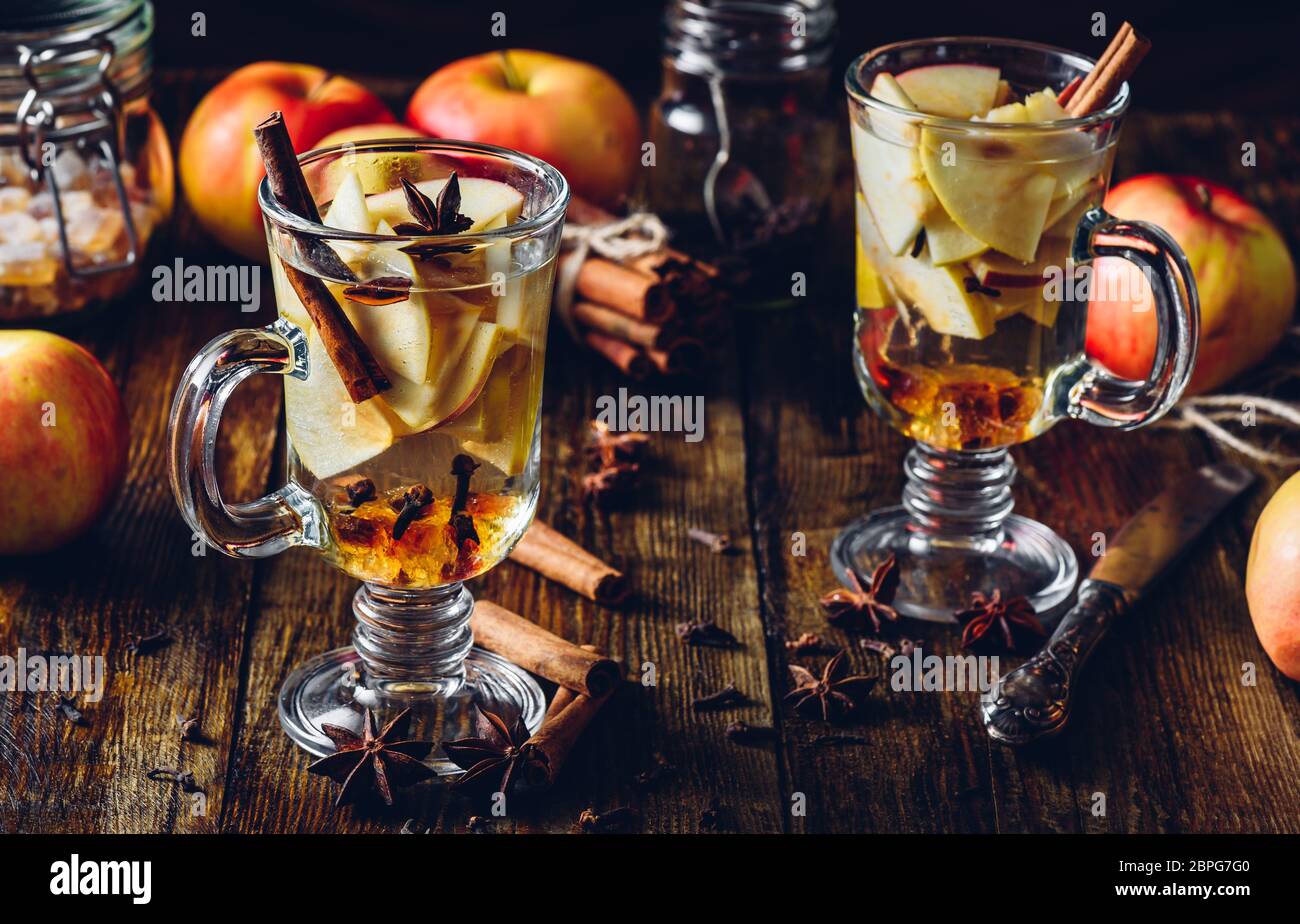 Deux verres de boisson chaud Apple avec girofle, cannelle, étoile d'anis et de sucre candy. Tous les ingrédients et quelques ustensiles de cuisine sur table en bois. Banque D'Images