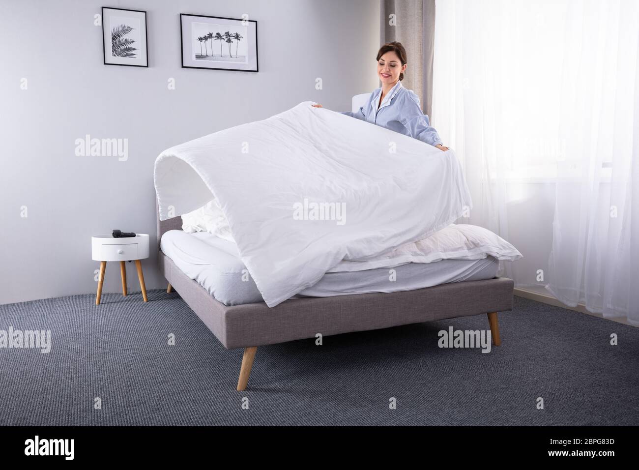 Souriante jeune femme de ménage organiser sur drap lit dans chambre d'hôtel Banque D'Images