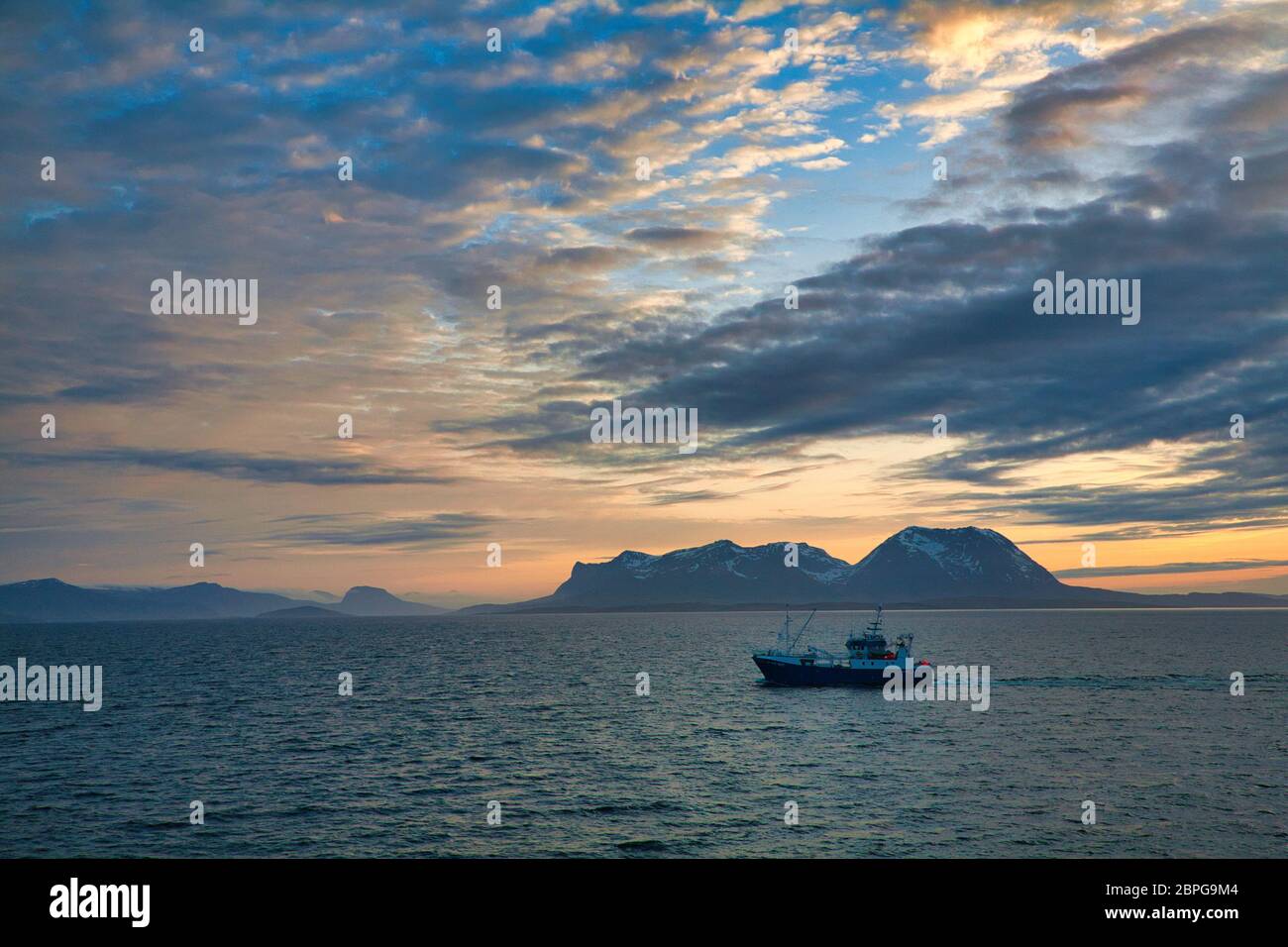 Îles au large de la côte ouest de la Norvège septentrionale, vues par la lumière du soleil de minuit avec un ciel spectaculaire, des nuages et un petit bateau de pêche en premier plan Banque D'Images