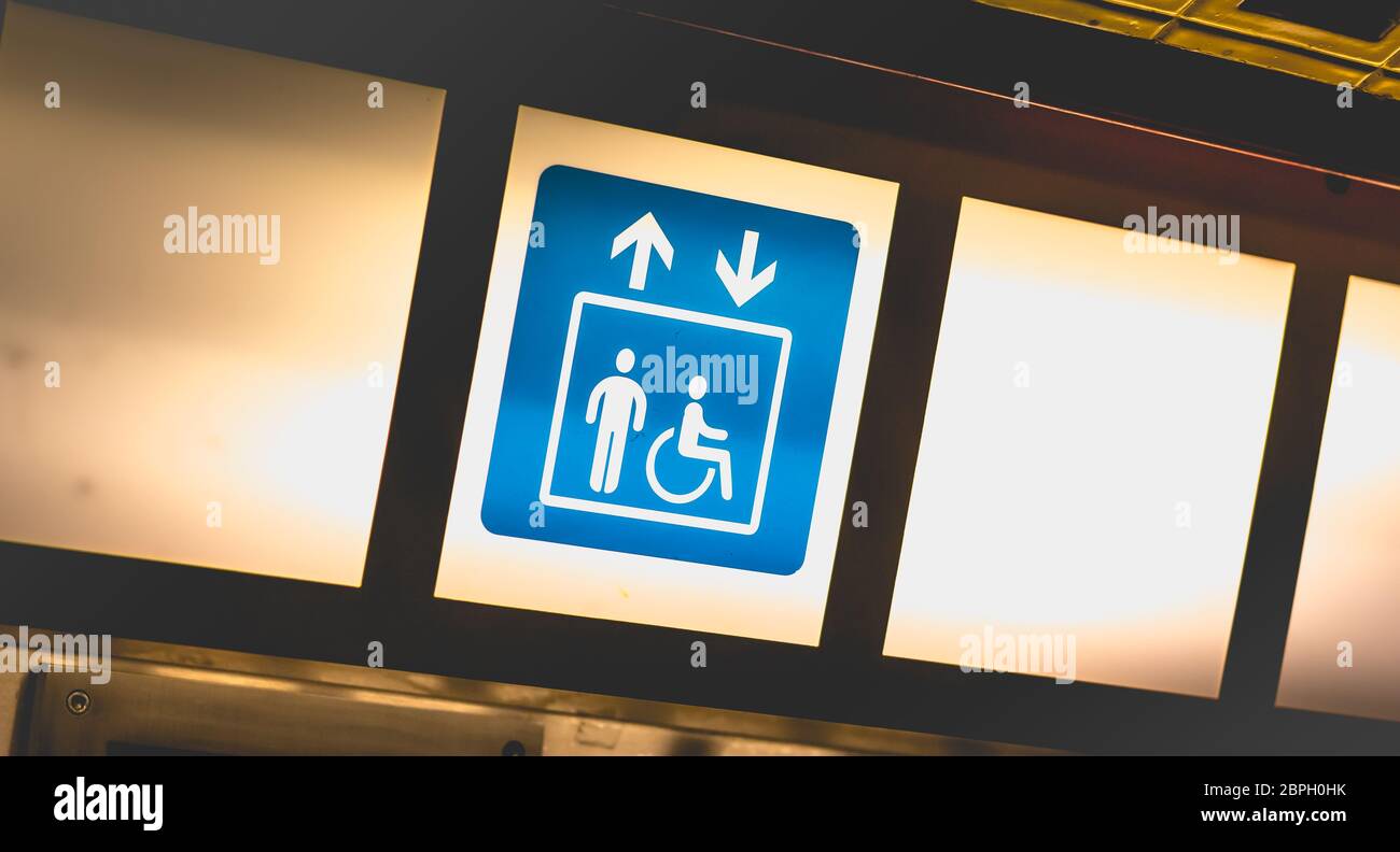Panneau bleu sur fond lumineux indiquant l'accès aux ascenseurs pour les personnes à mobilité réduite Banque D'Images