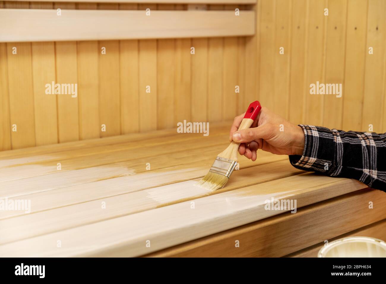 appliquer à la main de la cire de protection contre le bois sur le banc de sauna avec un pinceau Banque D'Images