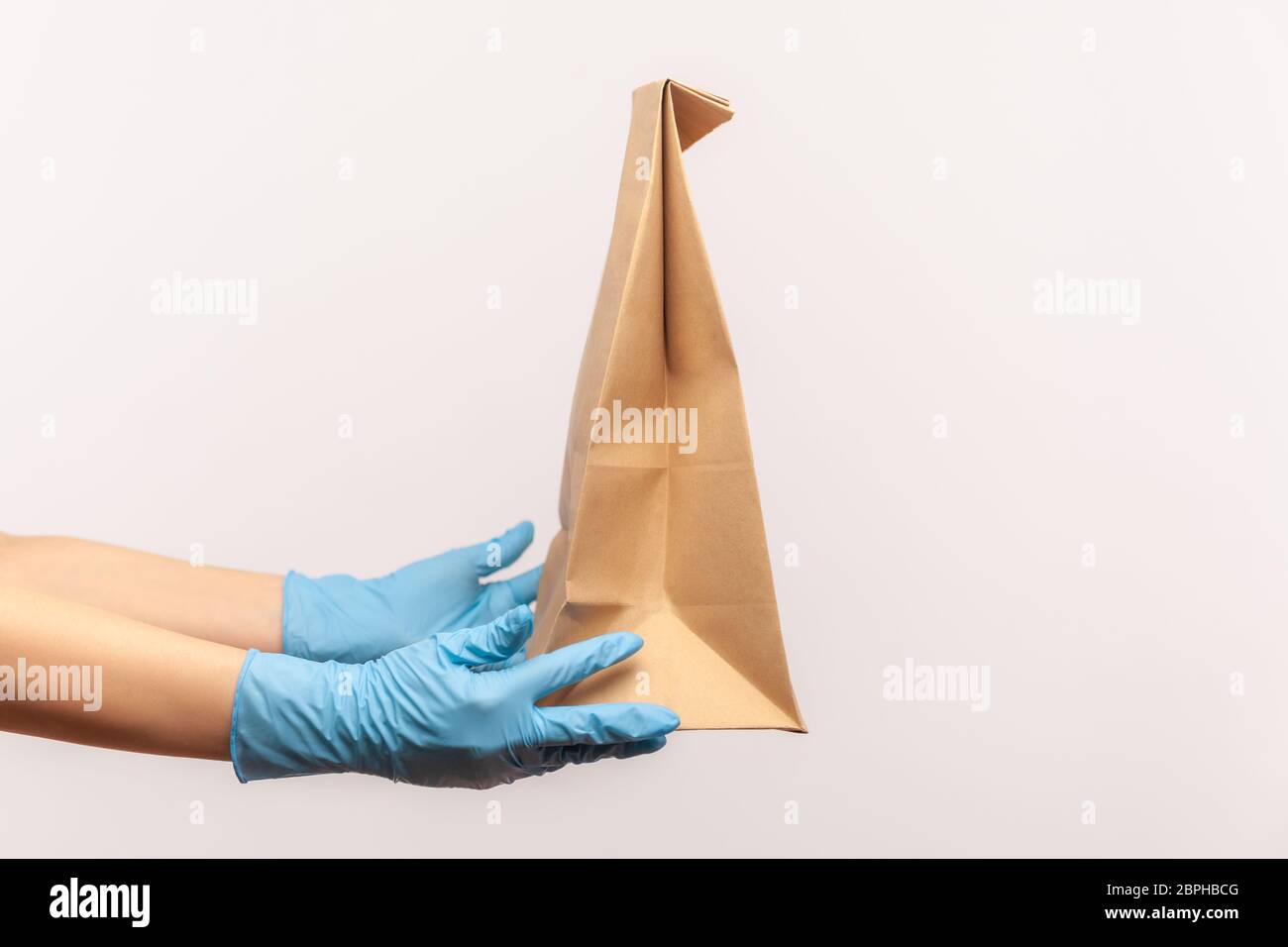 Vue latérale du profil gros plan de la main humaine dans des gants chirurgicaux bleus tenant et paquet de papier d'artisanat avec nourriture. Concept de livraison sûre de nourriture. Intérieur, studio s Banque D'Images