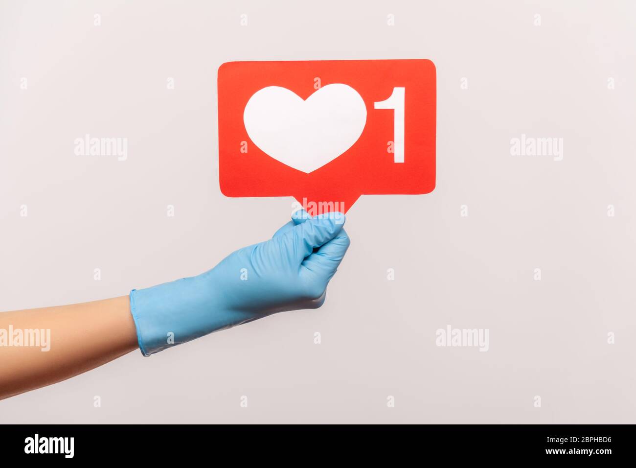 Vue latérale du profil gros plan de la main humaine avec des gants chirurgicaux bleus tenant les médias sociaux comme le bâton. En intérieur, prise de vue en studio, isolé sur fond gris. Banque D'Images