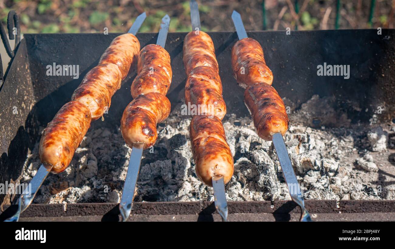 Les saucisses sont frites sur des brochettes sur des plats à base de charbon sur le gril. Préparer la nourriture pour un pique-nique. Banque D'Images