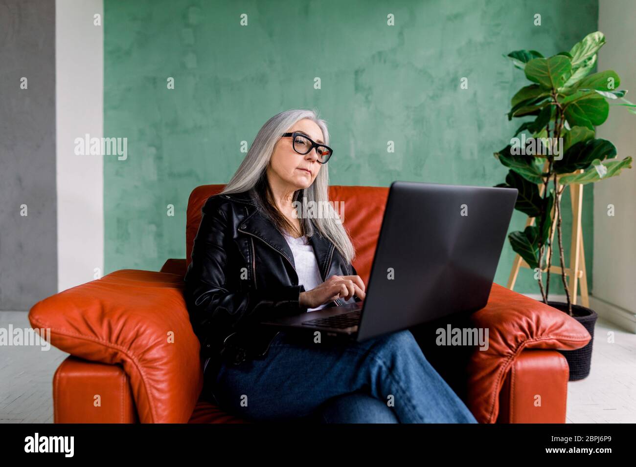 Portrait de belle femme âgée de 60 ans concentrée avec de longs cheveux  gris, portant des vêtements et des lunettes modernes et tendance, assis  dans un fauteuil rouge et Photo Stock - Alamy