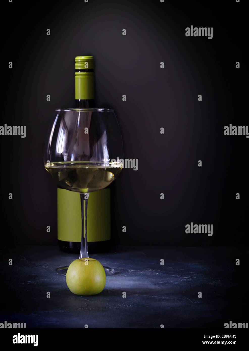 Une bouteille, un verre de vin blanc aux fruits et une pomme verte sur fond sombre Banque D'Images