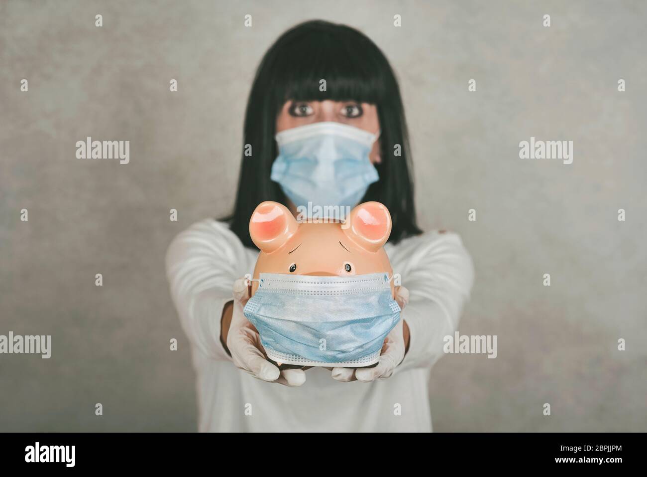femme portant un masque médical pour le coronavirus avec une porcgybank sur fond gris Banque D'Images