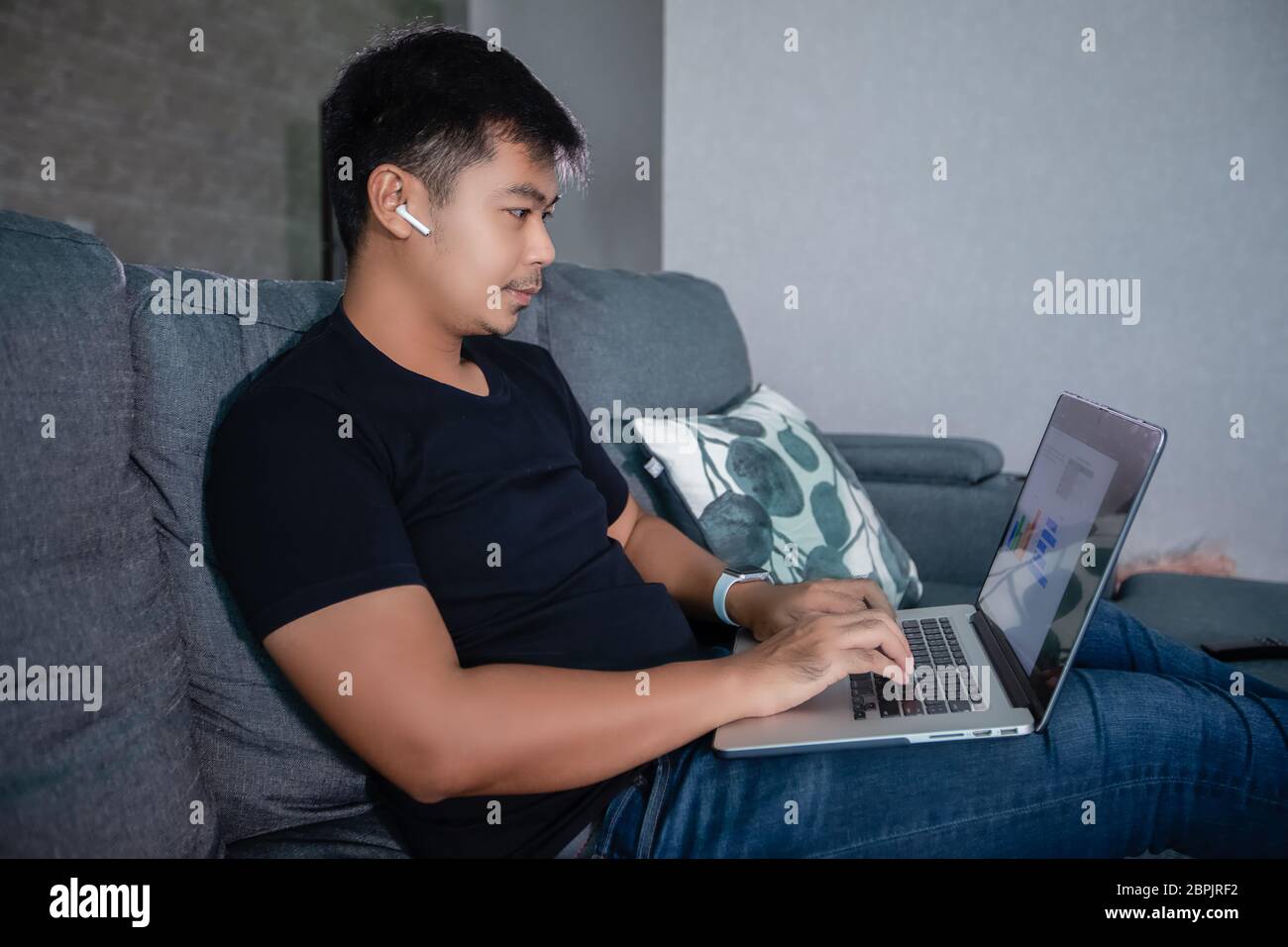 Homme d'affaires asiatique utilisant des écouteurs sans fil et utilisant ordinateur portable travaillant à domicile.il prépare des graphiques et des informations pour les réunions en ligne à h Banque D'Images