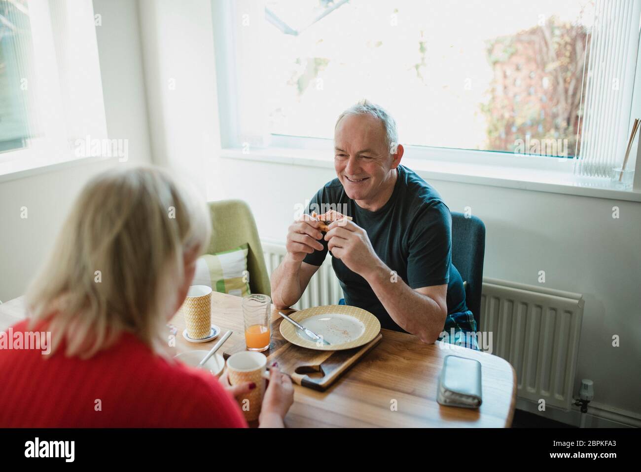 Man est en train de rire et de parler avec son partenaire, alors qu'ils prendre le petit-déjeuner ensemble à la maison. Banque D'Images
