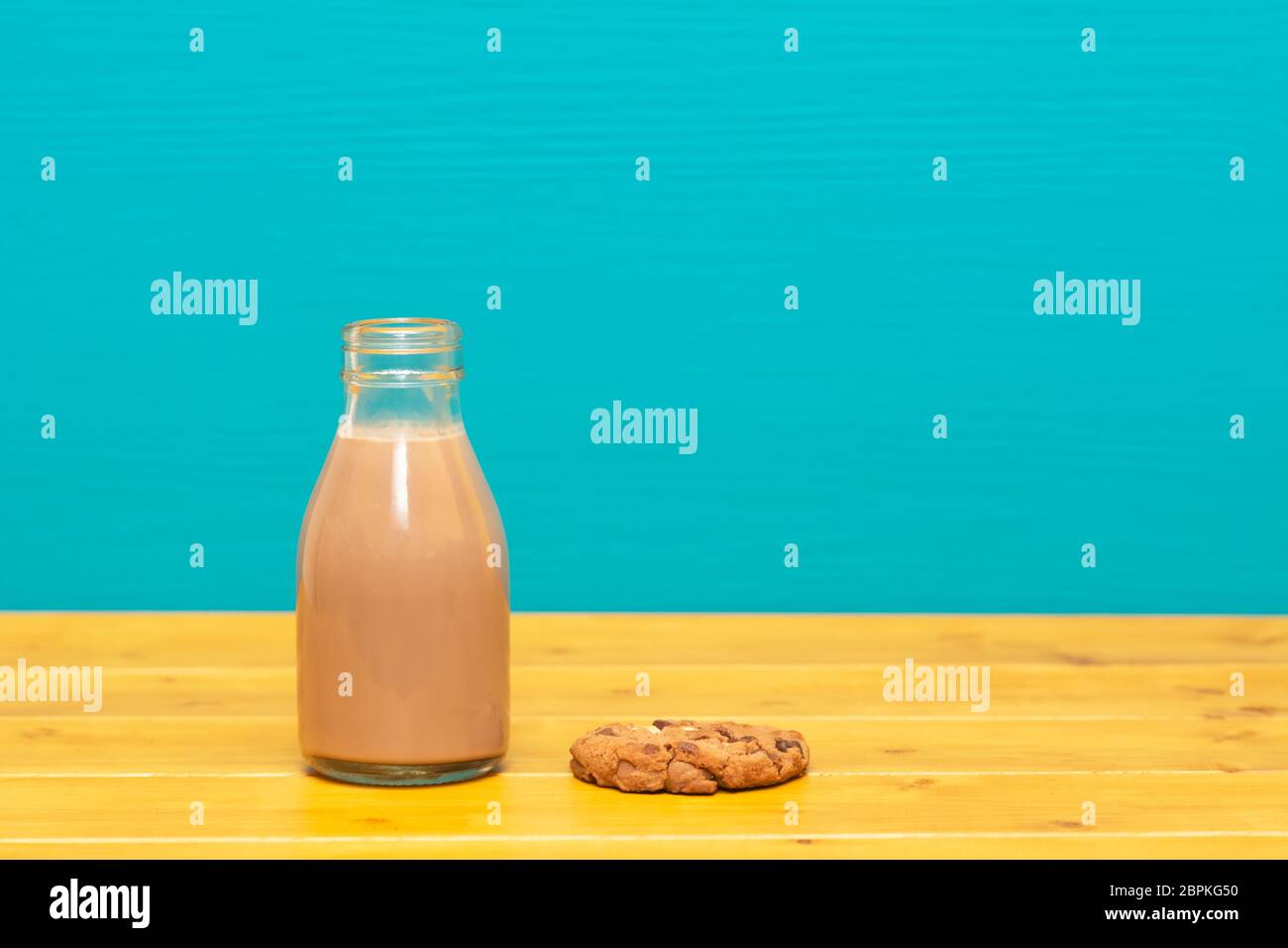 Lait frappé au chocolat dans un style rétro un tiers de pinte de lait en verre bouteille et d'un biscuit aux brisures de chocolat, sur une table de bois contre un lumineux peint sarcelles backgroun Banque D'Images