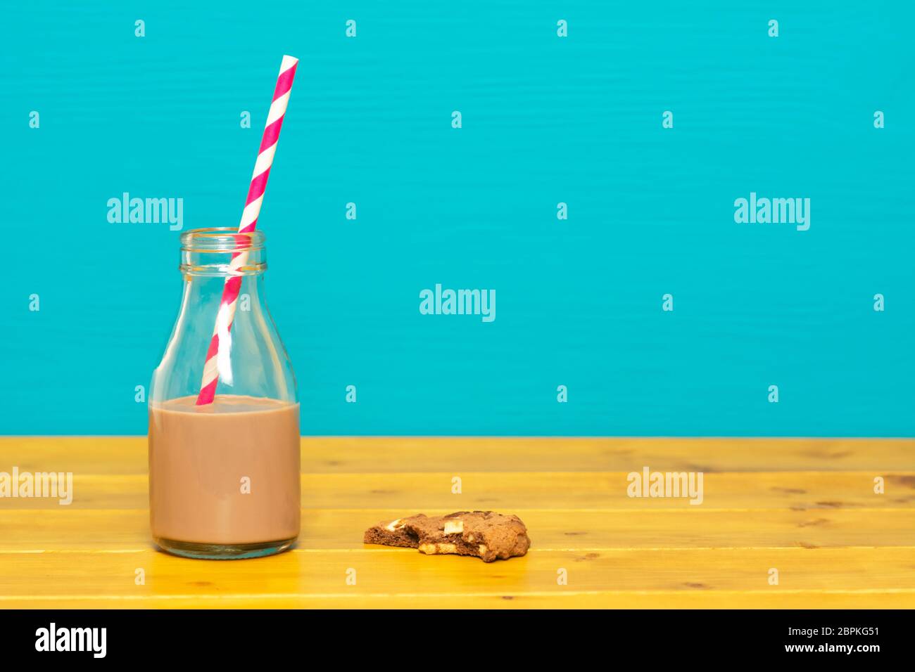 Un tiers de pinte de lait en verre bouteille à moitié pleine du chocolat avec avec une paille rétro et une demi-biscuit aux brisures de chocolat mangé, sur une table en bois nouveau Banque D'Images