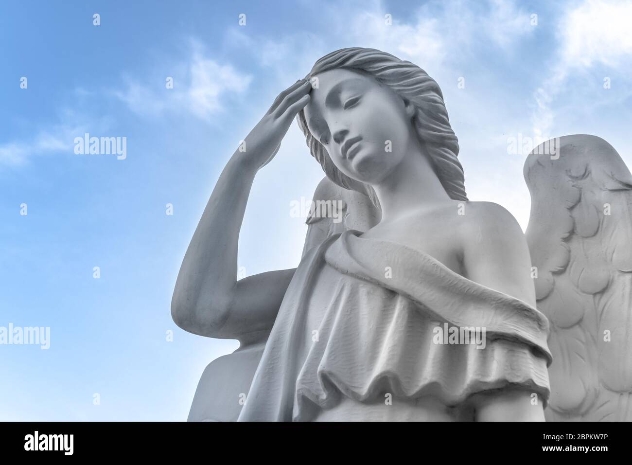 Ancienne statue d'un ange de la paix avec la main avec la main sur le front. La sculpture antique. Sur un fond de ciel bleu avec des nuages blancs. Idéal Banque D'Images