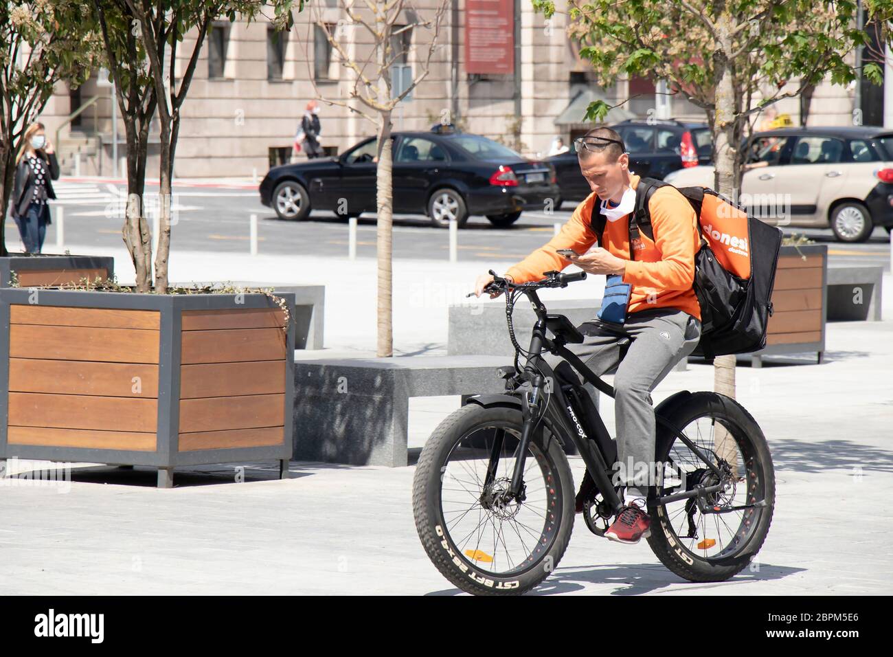 Belgrade, Serbie - 5 mai 2020 : un service de livraison de jeune ville de messagerie à vélo électrique sur la place de la ville tout en regardant le téléphone portable Banque D'Images