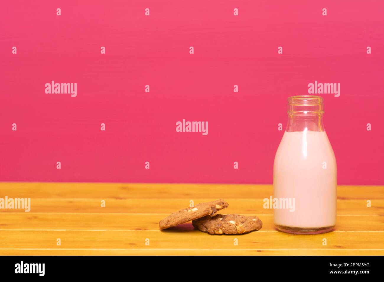 Lait frappé aux fraises dans un tiers de pinte de lait en verre bouteille et d'un biscuit aux brisures de chocolat, sur une table de bois contre un arrière-plan peint rose Banque D'Images