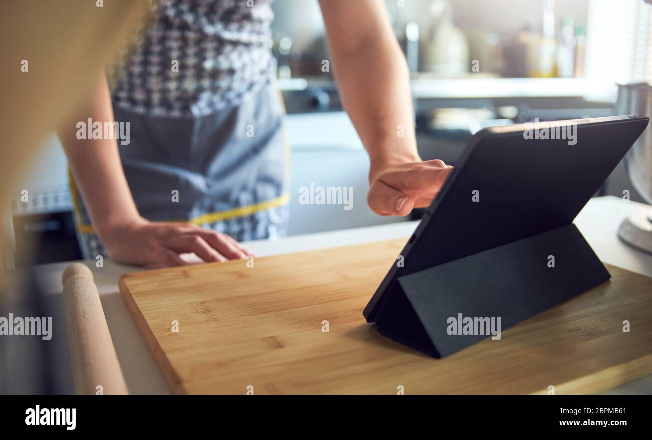 Femme utilisant un écran tactile sur une tablette numérique dans la cuisine à la maison sur une planche à découper Banque D'Images