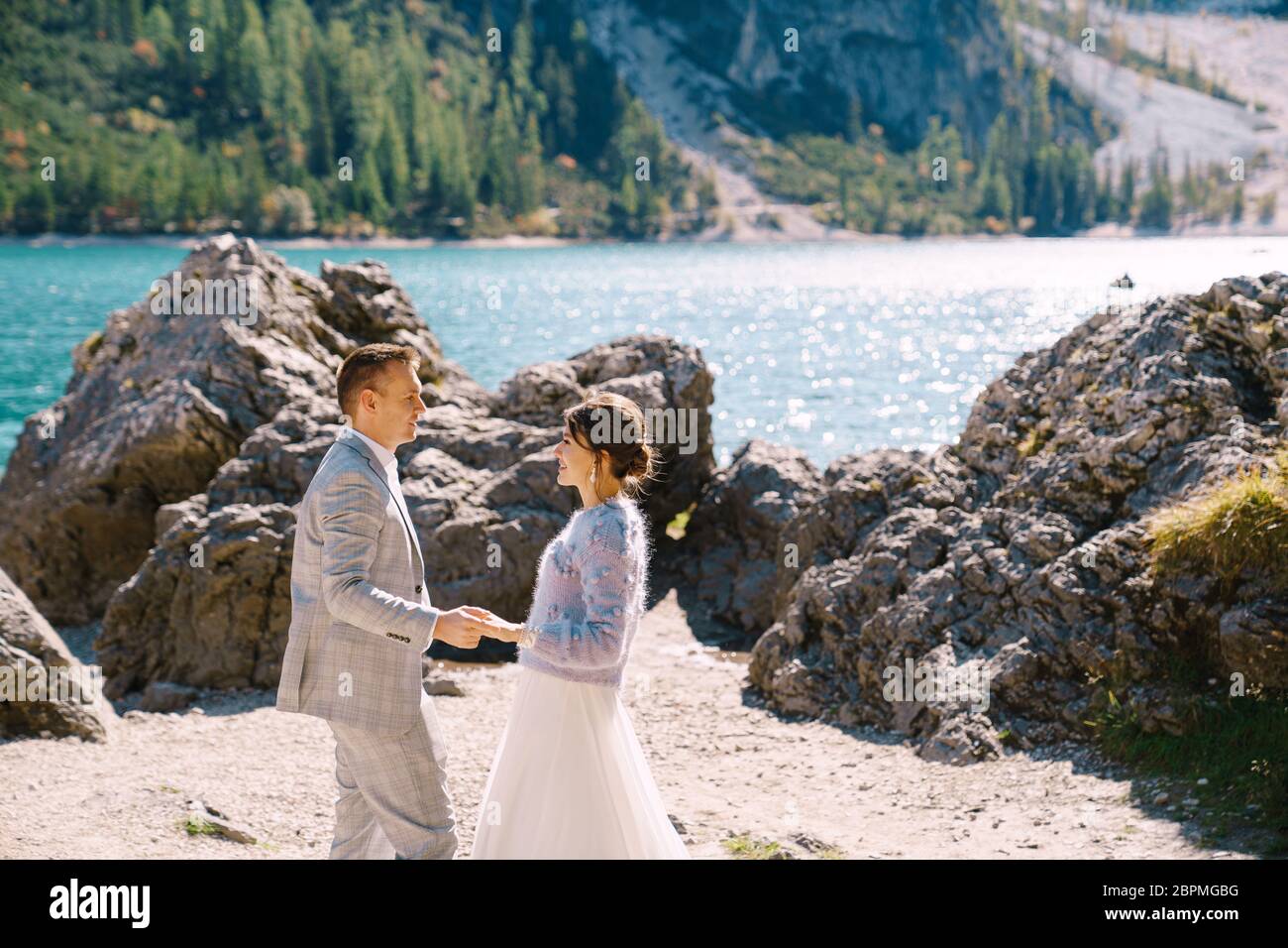 Les mariés se tiennent sur fond de pierres surplombant Lago di Braies en Italie. Mariage de destination en Europe, sur le lac de Braies. Aimant Banque D'Images