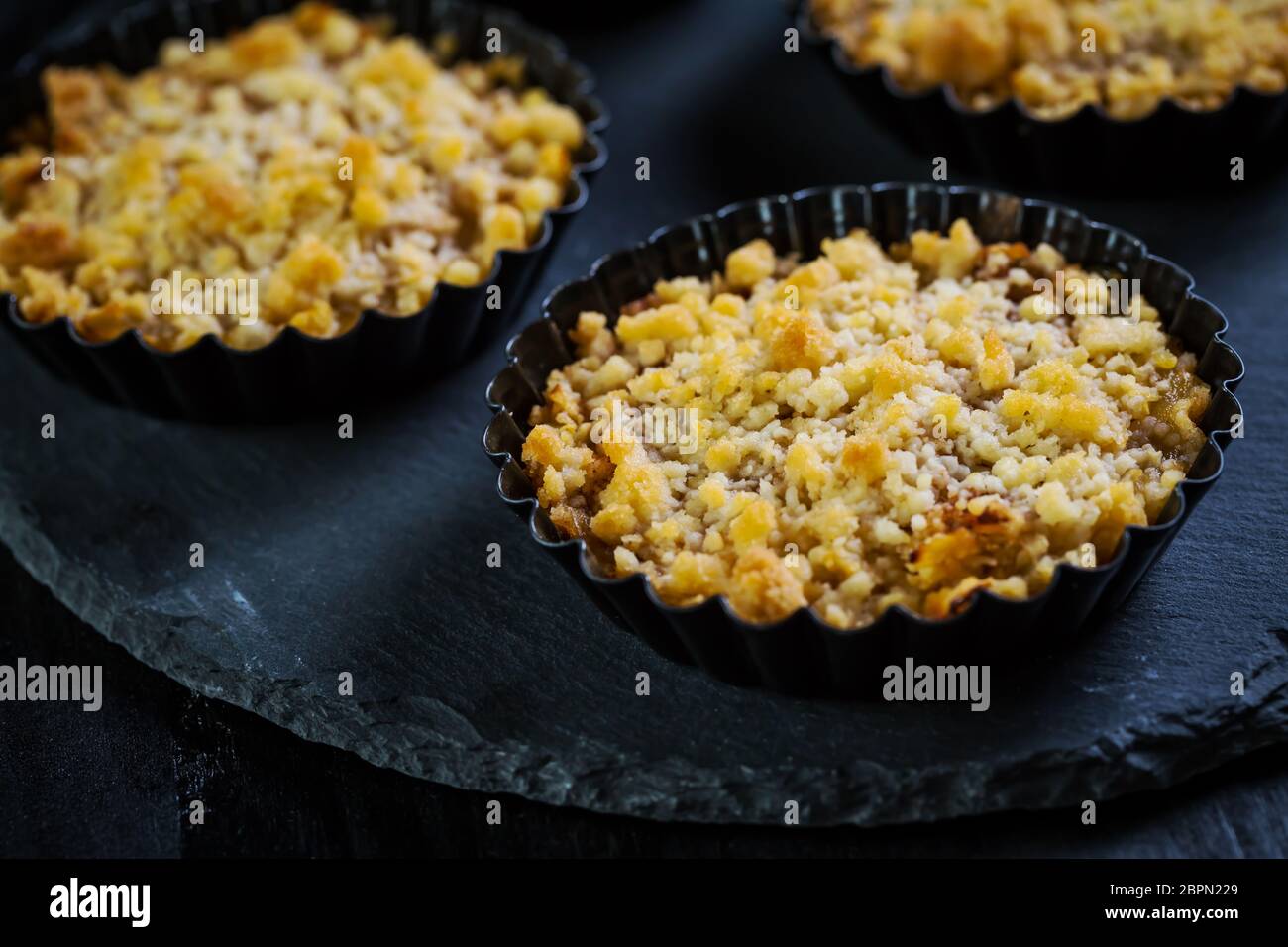 Petites et délicieuses tartes aux pommes ou crumble aux pommes sur fond noir. Tarte aux pommes. Banque D'Images
