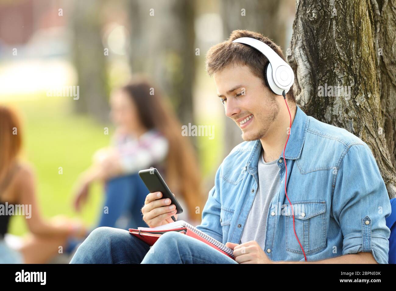 L'apprentissage des élèves à l'écoute tutoriels audio dans un parc assis sur l'herbe dans un parc Banque D'Images