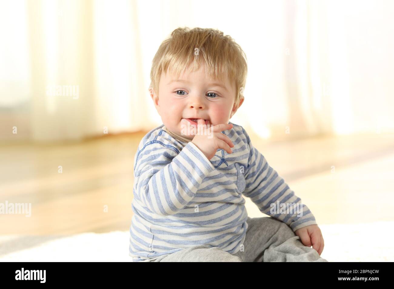 Portrait d'un enfant distrait de mordre un doigt assis sur le plancher Banque D'Images