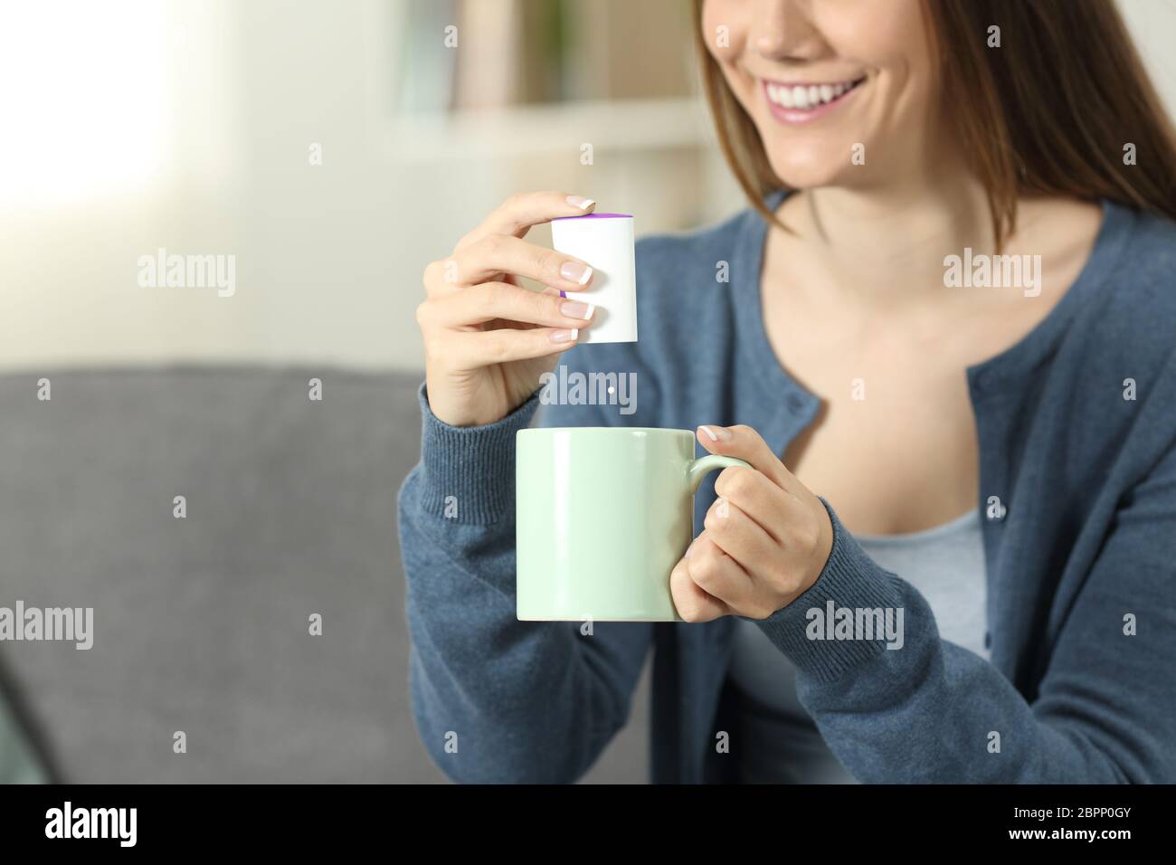 Gros plan d'une femme jetant mains sacharine comprimé dans un mug assis sur un canapé dans la salle de séjour à la maison Banque D'Images