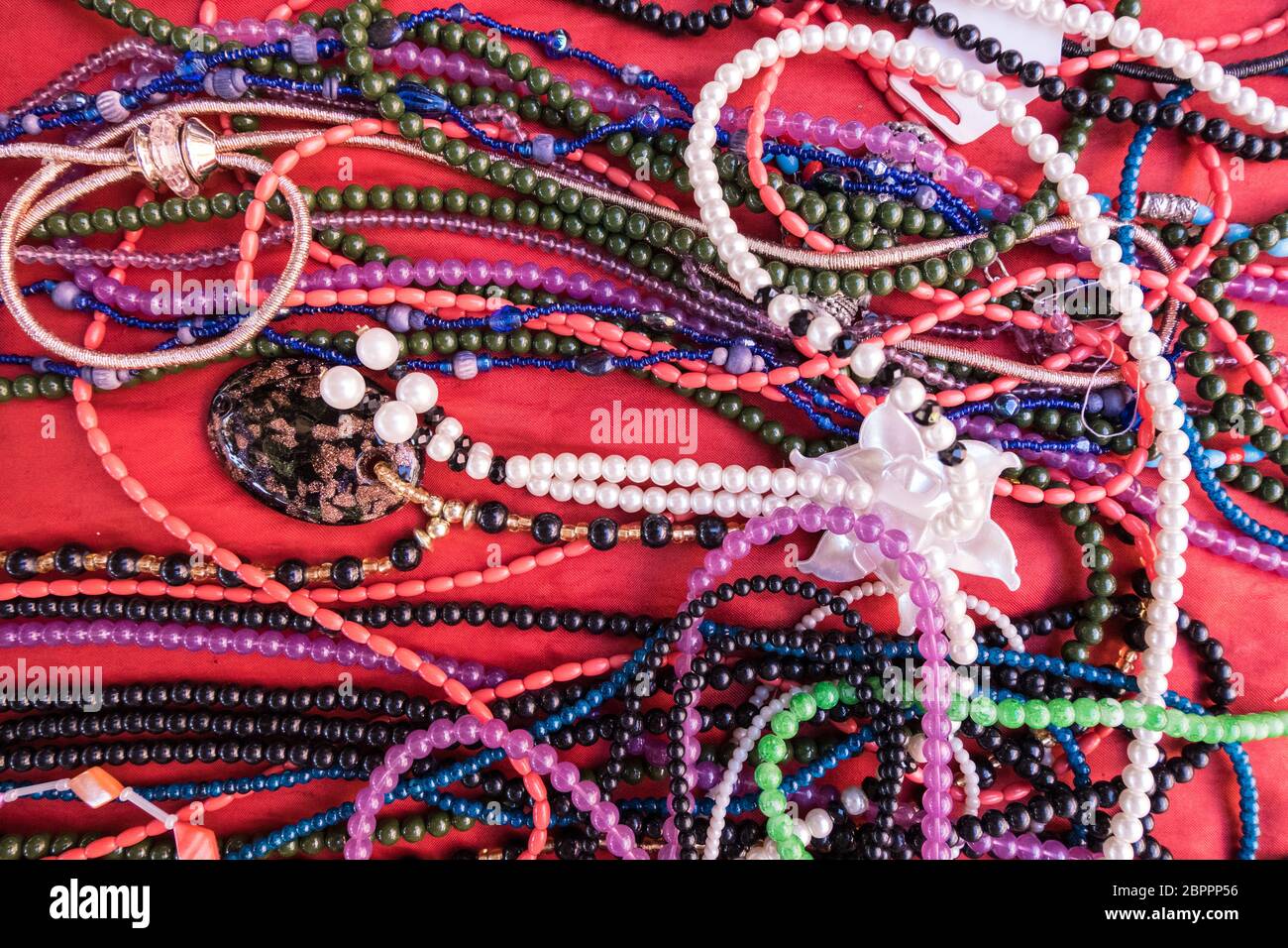 Image de fond de bracelets et colliers colorés à vendre à un marché aux puces avec fond en velours rouge. Banque D'Images