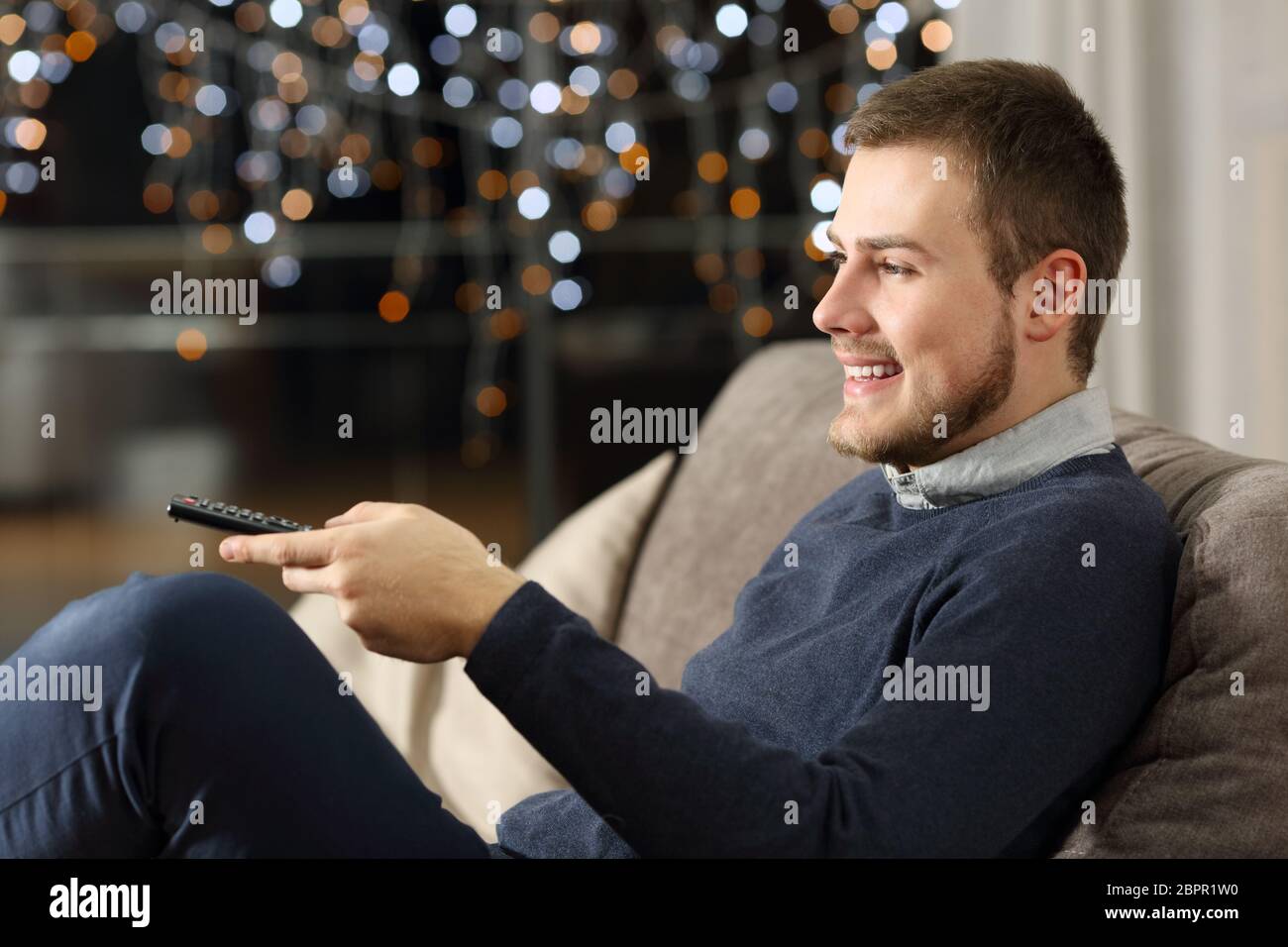 Homme heureux de regarder la télévision à la maison dans la nuit, assis sur un canapé dans la salle de séjour à la maison Banque D'Images