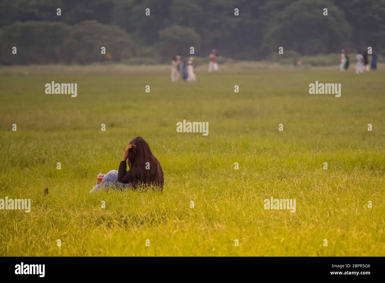 Jolie, joyeuse fille assise sur l'herbe verte et silences. Une jeune femme ou fille sur le pré vert à regarder et apprécier la nature soirée d'été. Maison de vacances eve Banque D'Images