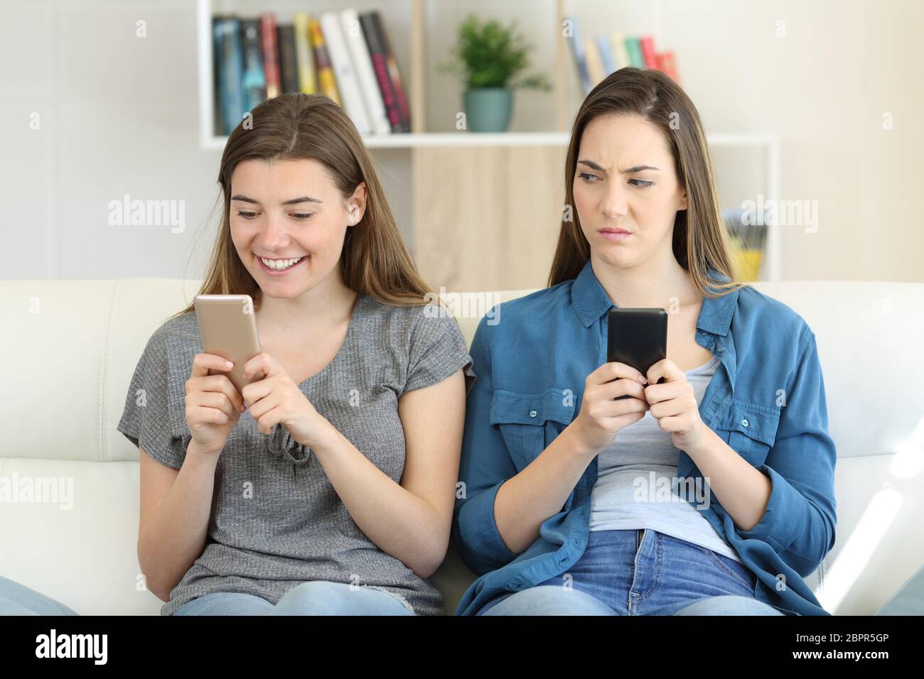 Envieux woman texting son amie dans un téléphone assis sur un canapé dans la salle de séjour à la maison Banque D'Images