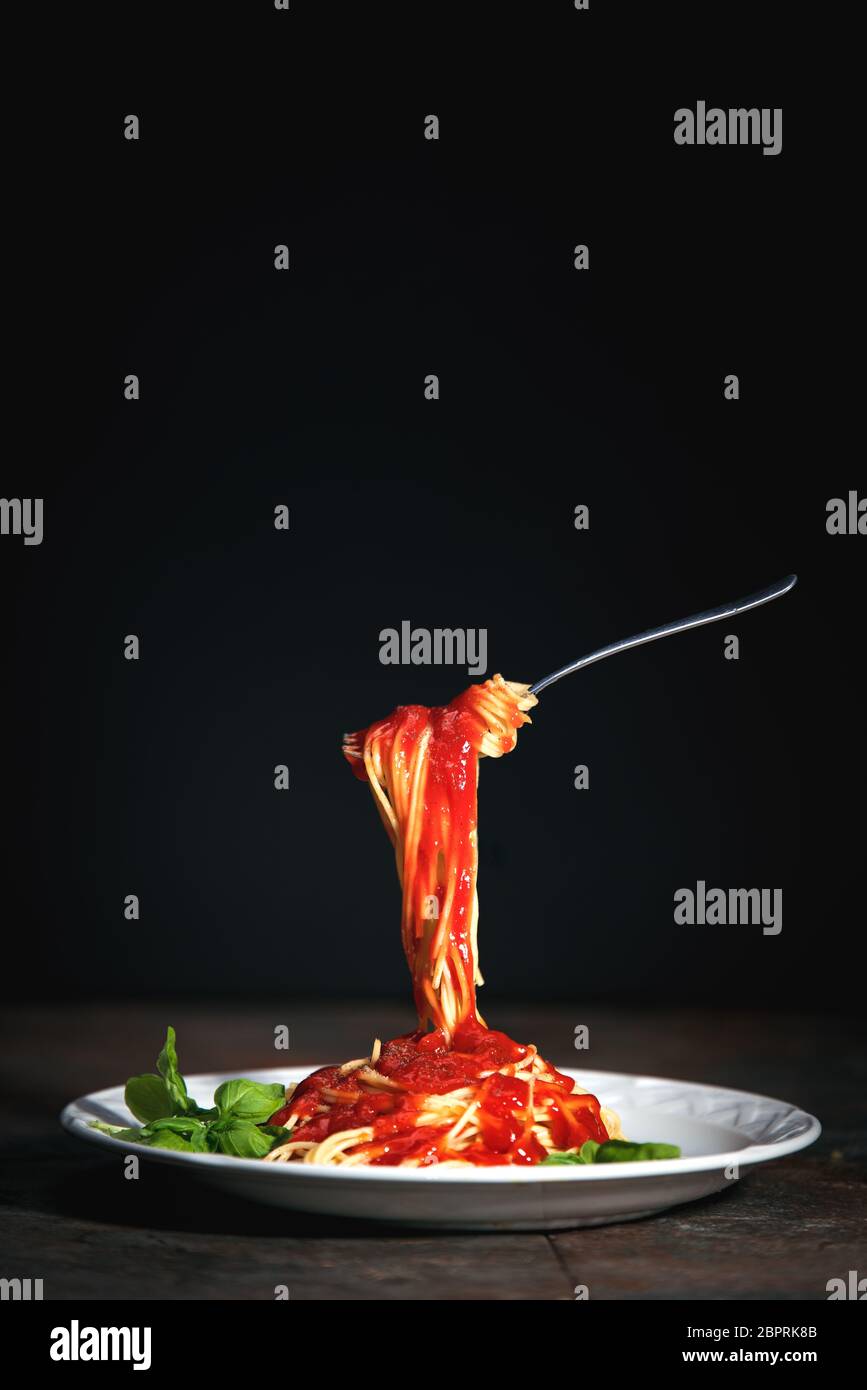 Savoureuses pâtes traditionnelles italiennes spaghetti appétissantes avec sauce tomate, parmesan au fromage et basilic sur une assiette sur table sombre Banque D'Images