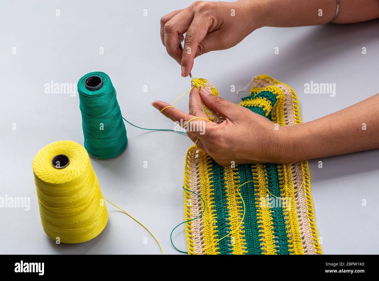 une femme faisant un motif de fil avec des fils jaunes et verts à l'aide d'un crochet crochet en crochet Banque D'Images