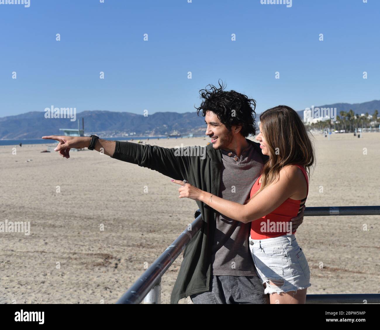 Un jeune couple heureux à la plage pointant vers quelque chose au loin Banque D'Images