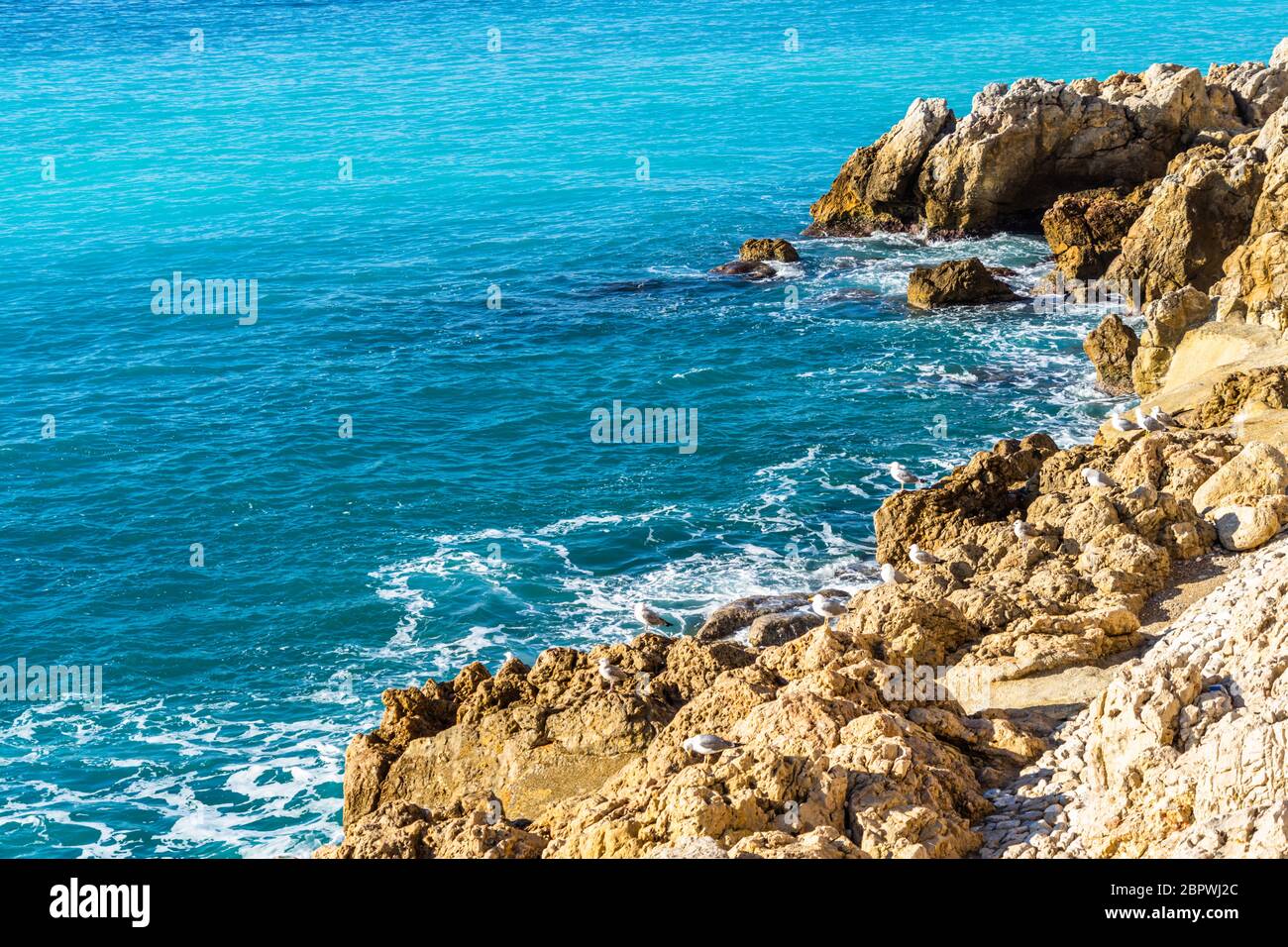 L'eau turquoise de la mer Méditerranée aglamant les rochers près du bord de mer de Nice, France Banque D'Images