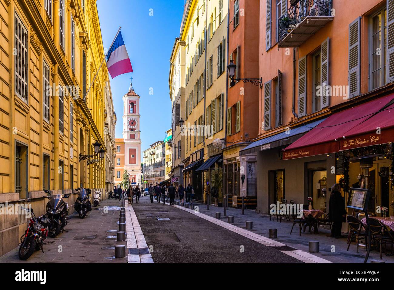 Nice, France, janvier 2020 – UNE rue piétonne typique de la vieille ville de Nice avec un drapeau français provenant d'un bâtiment et de la tour de l'horloge du Palais Rusca Banque D'Images