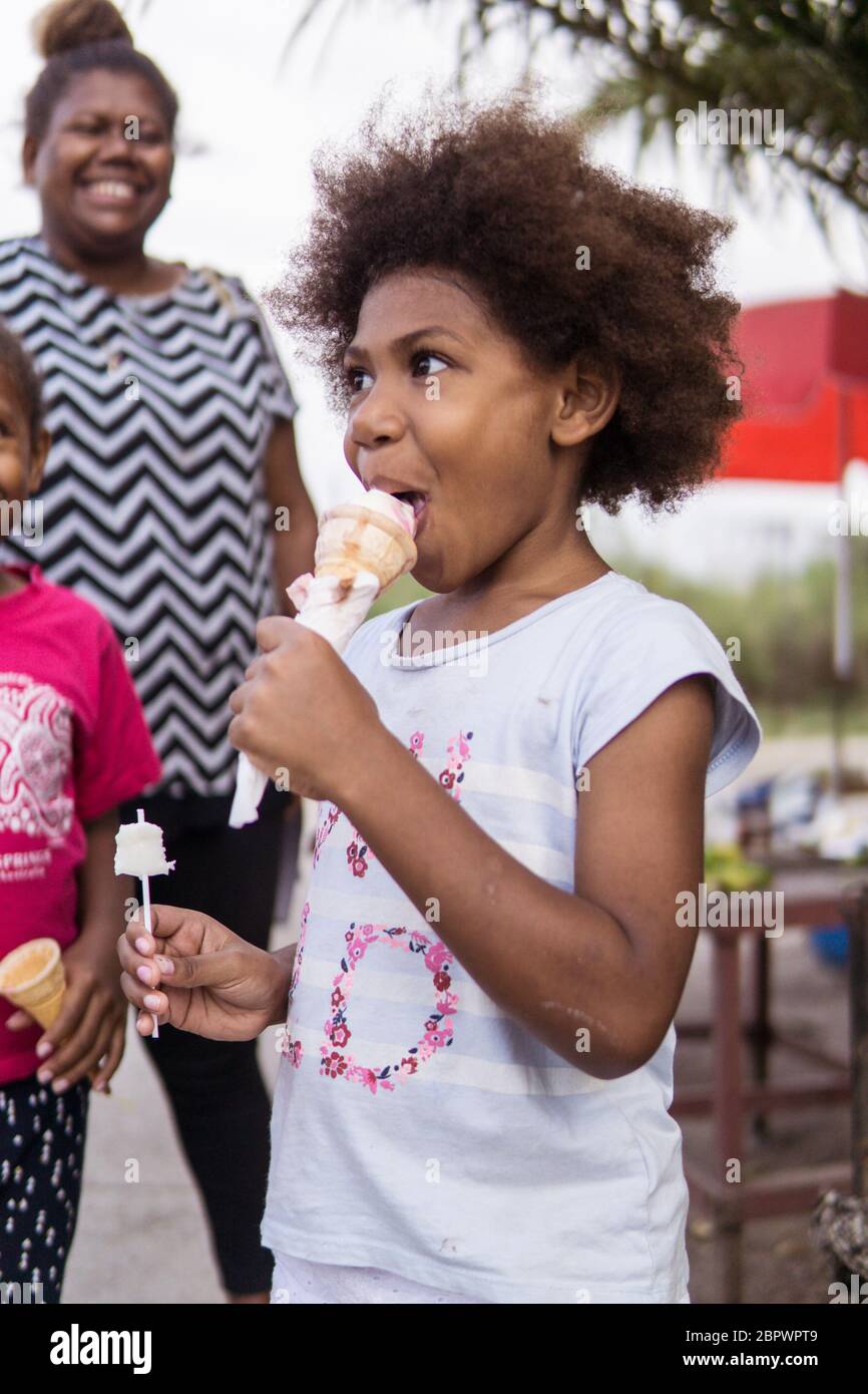 Port Moresby / Papouasie-Nouvelle-Guinée: Un garçon de Papouasie avec des cheveux afro qui mangent de la glace avec des gens souriants Banque D'Images
