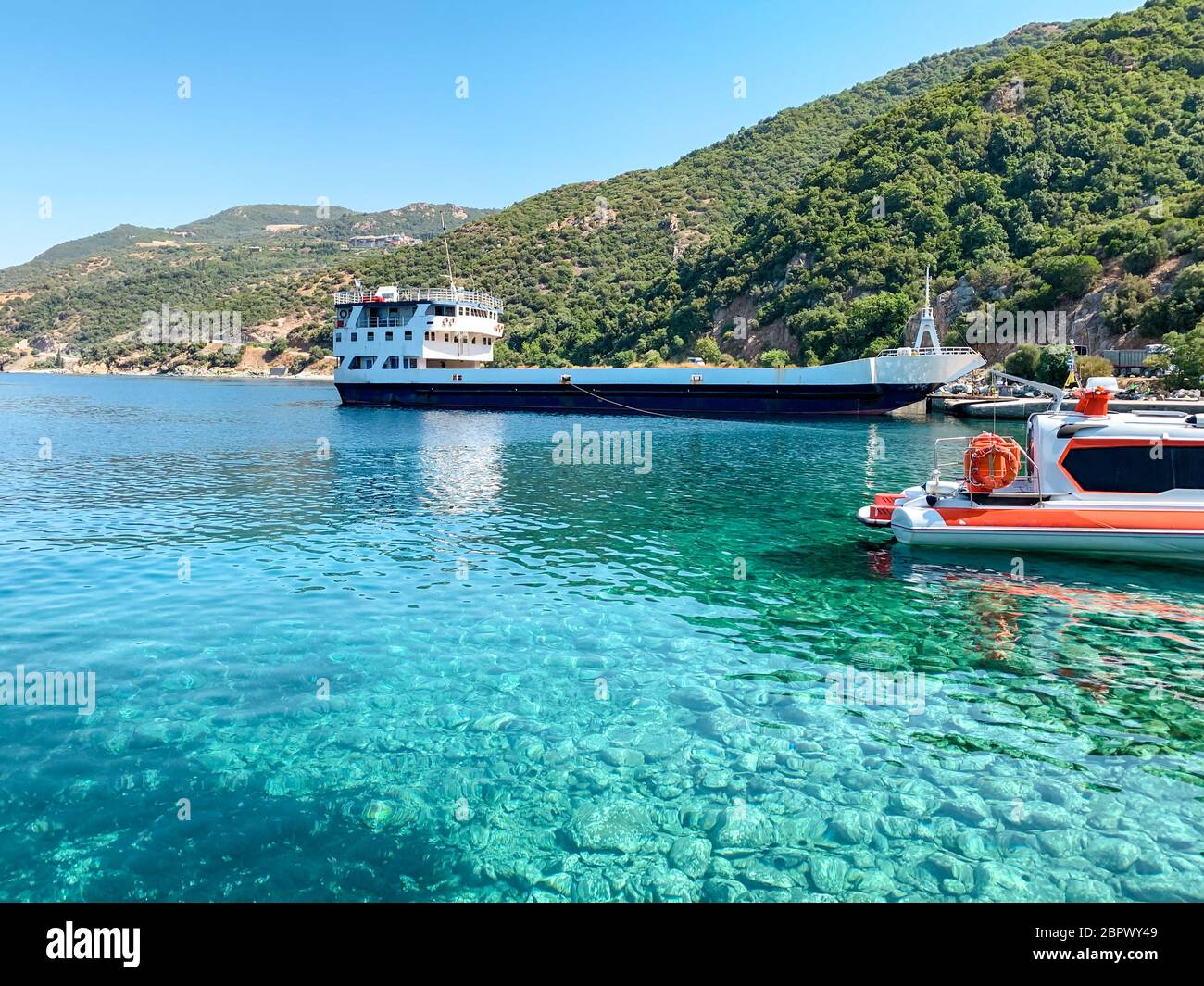 Un quai au pied du Mont Athos en Grèce. Eau de mer claire, un cargo sec, un petit bateau et une forêt en arrière-plan Banque D'Images
